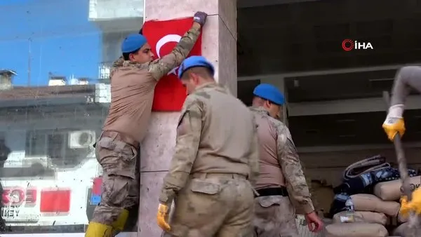 Mehmetçik, çamurun içerisinden çıkardığı Türk Bayrağı'nı temizleyerek duvara astı
